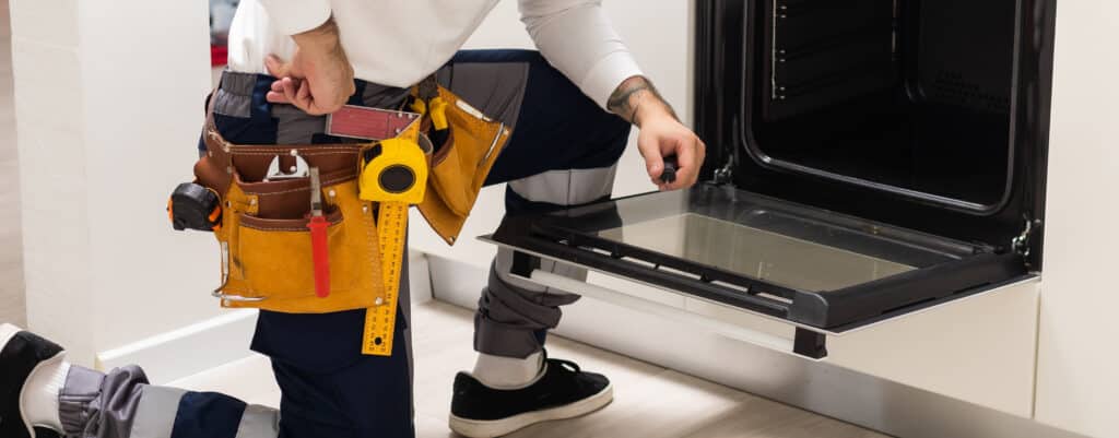 Professional serviceman repairing modern oven in kitchen